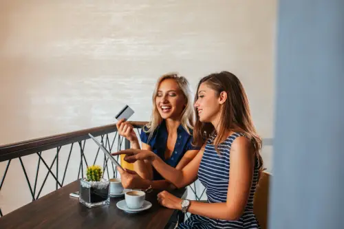 Dua perempuan yang sedang tertawa di sebuah kedai kopi, salah satunya memegang kartu kredit